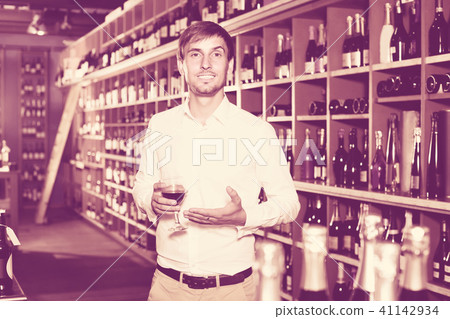 portrait of glad male customer tasting wine before purchasing it in wine store 41142934