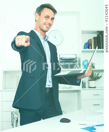 employee standing with laptop in office. 41143045