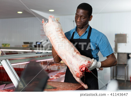 Skillful African American butcher processing carcase of young lamb for sale at butchery Skillful African American butcher processing carcase of young lamb for sale at butchery 41143647