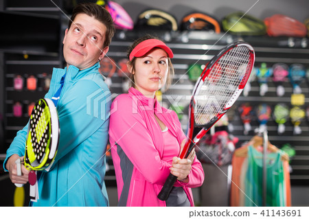 happy female with male are standing in sportwear with new racket for padel and tennis in the speciality store 41143691