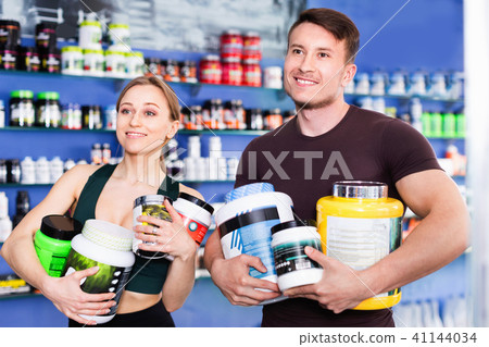 Happy young sporty people standing in store, holding big can of sport nutrition 41144034