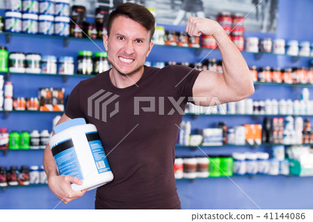 Athletic man with jar of sport nutrition supplements showing muscles Athletic man with jar of sport nutrition supplements showing muscles 41144086