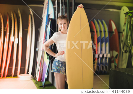 Woman is posing with surfboard in store on the beach. Woman is posing with surfboard in store on the beach. 41144089