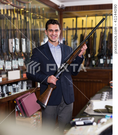 Positive salesman in hunting shop demonstrating shotgun Positive salesman in hunting shop demonstrating shotgun 41144090