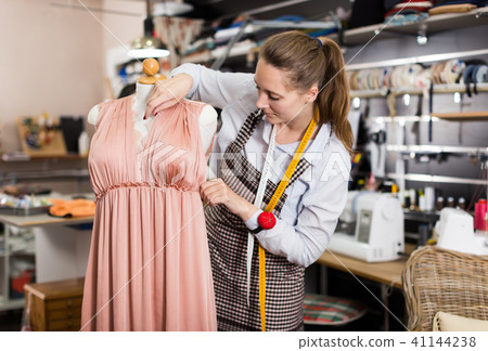 Female seamstress is thinking about new dress for collection of clothes near mannequin Female seamstress is thinking about new dress for collection of clothes near mannequin 41144238
