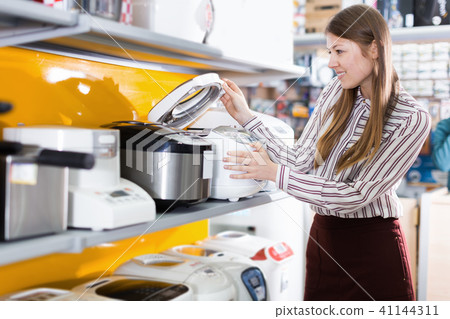 Young positive female housewife choosing multicooker Young positive female housewife choosing multicooker 41144311