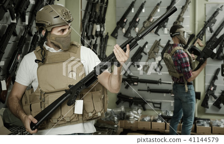 Young guys in military equipment with rifle in airsoft shop Young guys in military equipment with rifle in airsoft shop 41144579
