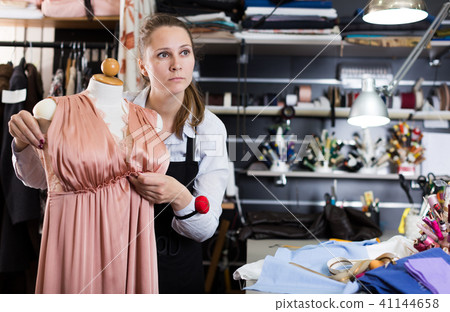 Female standing near mannequin with dress at sewing workshop Female standing near mannequin with dress at sewing workshop 41144658