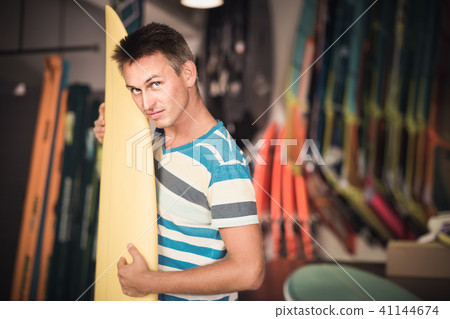 male is posing with surfboard in store on the beach. male is posing with surfboard in store on the beach. 41144674