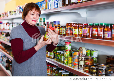 female buyer choosing canned jar of tomato paste at the supermarket 41144829
