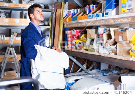 Sellerman in uniform is putting bags on the shelves in the building store. Sellerman in uniform is putting bags on the shelves in the building store. 41146204