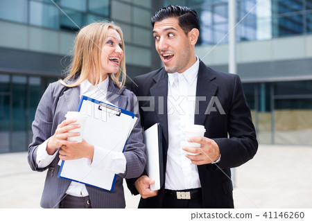 Businessman and his woman colleague in suit are standing with folder and coffee Businessman and his woman colleague in suit are standing with folder and coffee 41146260