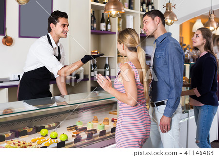 Cheerful seller helping friends to choose sweets Cheerful seller helping friends to choose sweets 41146483