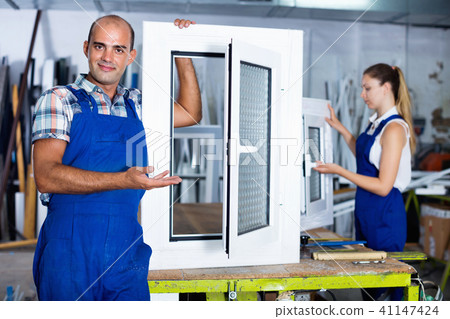 Confident man in workwear with finished window from pvc profile at workplace Confident man in workwear with finished window from pvc profile at workplace 41147424