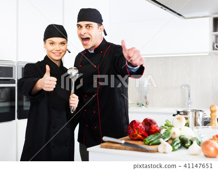 Man and woman kitcheners in uniform are standing with devices in the kitchen Man and woman kitcheners in uniform are standing with devices in the kitchen 41147651