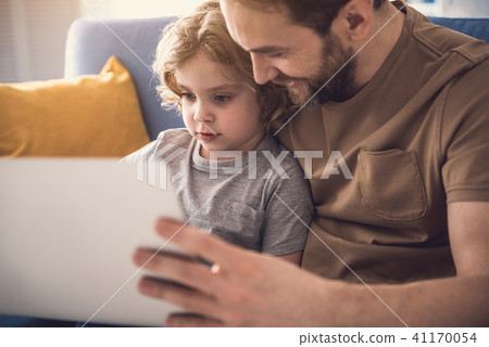Grinning dad and little boy are watching something on laptop Grinning dad and little boy are watching something on laptop 41170054