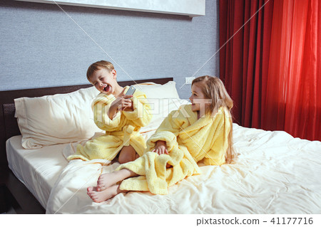 Happy laughing kids, boy and girl in soft bathrobe after bath play on white bed Happy laughing kids, boy and girl in soft bathrobe after bath play on white bed 41177716