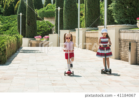 Preschooler girls riding scooter outdoors. 41184067