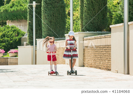 Preschooler girls riding scooter outdoors. 41184068