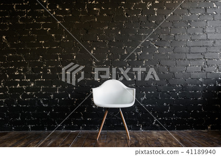 White chair standing in room on brown wooden floor over black brick wall White chair standing in room on brown wooden floor over black brick wall 41189940