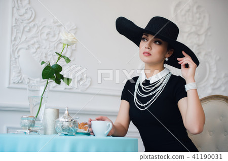 Woman in hat, much like the famous actress, croissant eating and drinking tea. 41190031