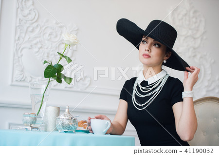 Woman in hat, much like the famous actress, croissant eating and drinking tea. 41190032