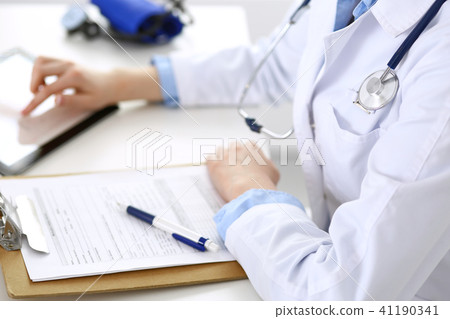 Woman doctor using tablet computer while sitting at the desk in hospital closeup. Cardiologist 41190341