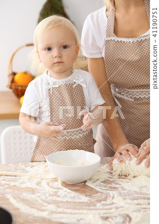 Little girl and her blonde mom in beige aprons  playing and laughing while kneading the dough in th 41190751