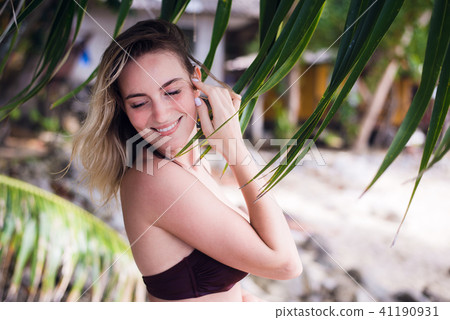 A beautiful young woman with long blonde hair posing on a beach dressed in sexy bikini top. She 41190931