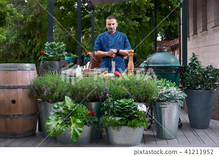 beautiful European-looking chef standing at restaurant terrace, slicing vegetables and looking at beautiful European-looking chef standing at restaurant terrace, slicing vegetables and looking at 41211952