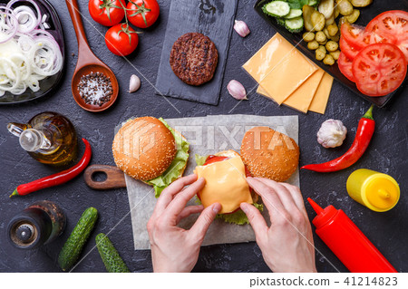 Image on top of two hamburgers, human hands and ingredients Image on top of two hamburgers, human hands and ingredients 41214823