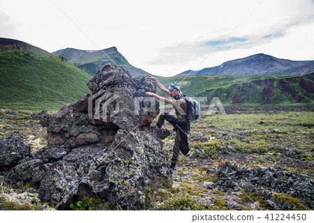 Hiker with backpack climbing up to frozen lava stone in voolcano valey. Beautiful mountain view. Hiker with backpack climbing up to frozen lava stone in voolcano valey. Beautiful mountain view. 41224450