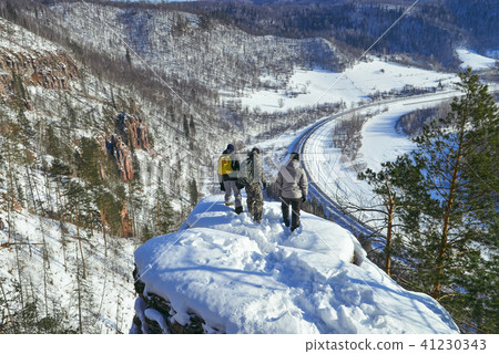 Group of people standing at mountain peak and looking down from high altitude at sunny winter day 41230343