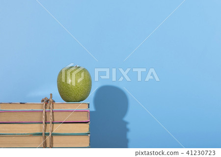Green apple and old books with shadow. Blue background. Green apple and old books with shadow. Blue background. 41230723
