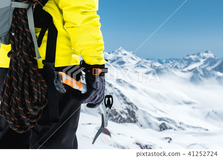 A mountaineer man holds an ice ax high in the mountains covered with snow. Close-up from behind A mountaineer man holds an ice ax high in the mountains covered with snow. Close-up from behind 41252724