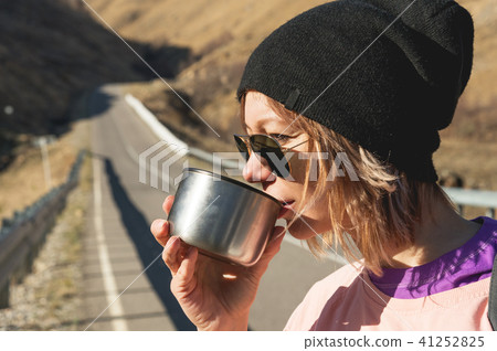 A hipster girl wearing sunglasses and a black hat is drinking tea or coffee from a mug from a A hipster girl wearing sunglasses and a black hat is drinking tea or coffee from a mug from a 41252825