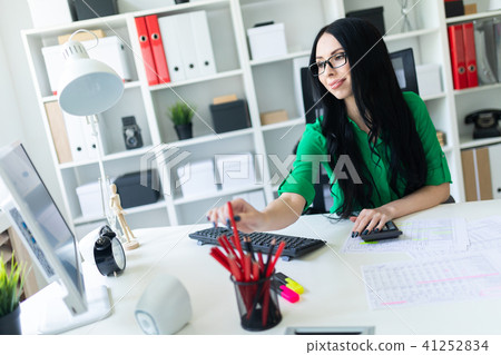 A young girl in glasses works in the office with a computer, a calculator and documents. 41252834