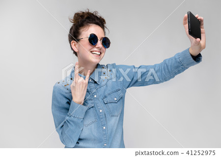 Young brunette girl in round glasses. Hairs are gathered in a bun. Girl with a black phone. The girl 41252975