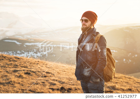 Fashion portrait of a bearded hipster young man wearing sunglasses, a backpack and hat on a 41252977