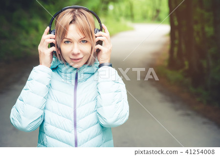Portrait of an attractive sports girl blonde in a light running down jacket dressing bluetooth Portrait of an attractive sports girl blonde in a light running down jacket dressing bluetooth 41254008