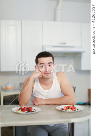 Young caucasian man sitting in kitchen near two plates with porridge and berries. 41263557