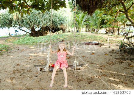 Cute female child riding on swing on sand background, wearing pink dress. 41263703