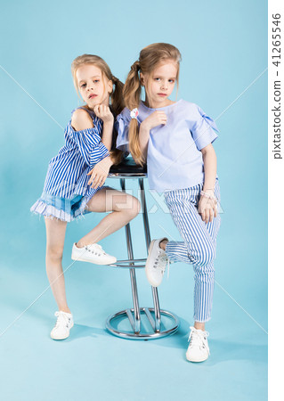 Girls twins in light blue clothes are posing near a bar stool on a blue background. Girls twins in light blue clothes are posing near a bar stool on a blue background. 41265546