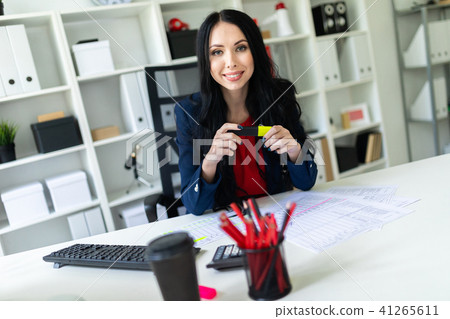 A beautiful young girl sits in the office at the table and holds a yellow marker in her hands. A beautiful young girl sits in the office at the table and holds a yellow marker in her hands. 41265611