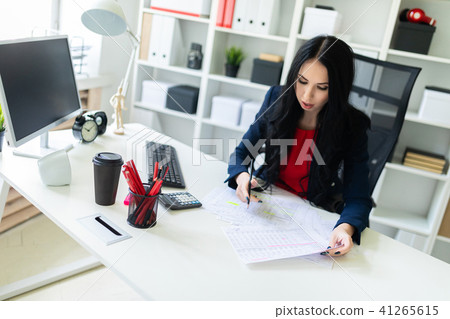 Beautiful young girl is working with documents in the office at the table and is holding a pencil in Beautiful young girl is working with documents in the office at the table and is holding a pencil in 41265615