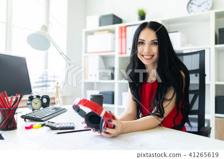 Beautiful young girl with headphones in hands is sitting in the office at the table. Beautiful young girl with headphones in hands is sitting in the office at the table. 41265619