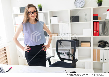Beautiful Young girl in the office is standing near the table and put her hands on her hips. Beautiful Young girl in the office is standing near the table and put her hands on her hips. 41265629