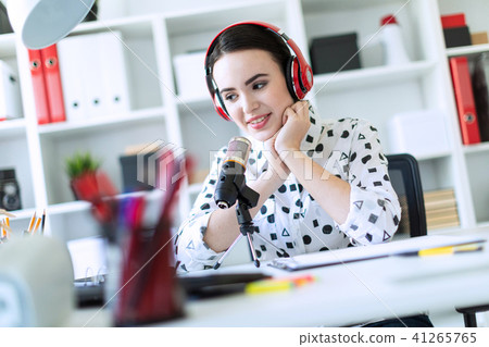 Beautiful young girl sitting in headphones and with microphone at table in office and talking. 41265765