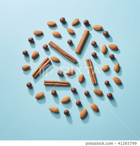 A circle of cinnamon sticks, almonds and chocolate balls on a blue paper background. Flat lay 41265799