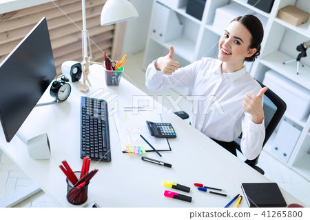 A young girl in the office sits at a table, works by documents and shows a class sign. 41265800
